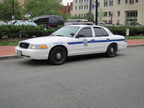 1991 Ford LTD Crown Victoria - Front-quarter view of a white Ford Crown Victoria police cruiser with a blue stripe and POLICE markings on a downtown street.