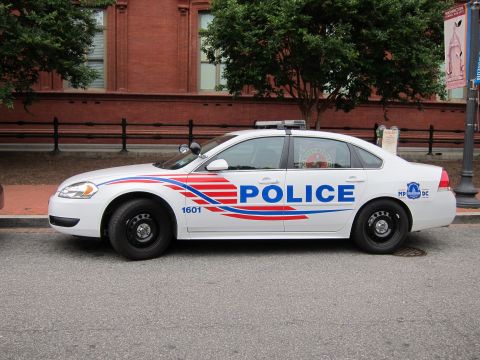 1991 Ford LTD Crown Victoria - Passenger-side profile of a white Chevrolet Impala DC police cruiser with POLICE markings parked beside a brick building.