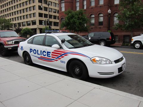 1991 Ford LTD Crown Victoria - Front-quarter view of a white Chevrolet Impala DC police cruiser with red-white-blue graphics parked on a sloped city street.