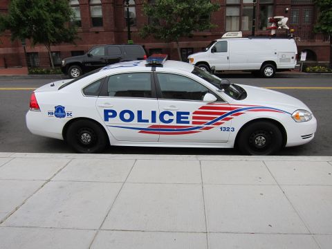1991 Ford LTD Crown Victoria - Driver-side profile of a white Chevrolet Impala DC police cruiser with red-and-blue striping parked at a city curb.