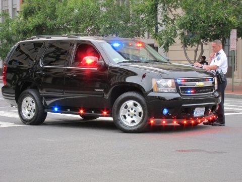 1991 Ford LTD Crown Victoria - Front-quarter view of a black Chevrolet Tahoe police SUV with flashing red and blue lights and an officer alongside.