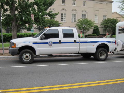 1991 Ford LTD Crown Victoria - white Ford Super Duty dually crew-cab police pickup with blue striping towing a trailer along a city street.