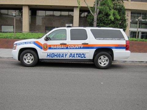1991 Ford LTD Crown Victoria - Driver-side profile of a white Nassau County Highway Patrol Chevrolet Suburban SUV with orange and blue stripes at a curb.