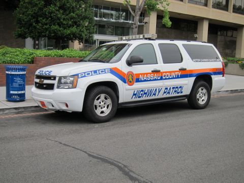 1991 Ford LTD Crown Victoria - Front-quarter view of a white Nassau County Highway Patrol Chevrolet Suburban police SUV with orange-blue striping on a street.