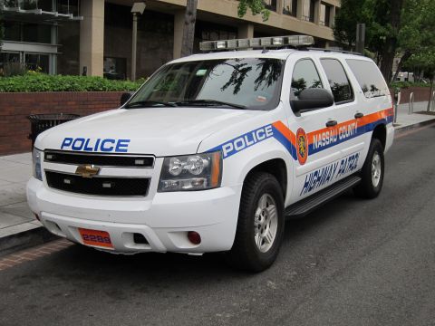 1991 Ford LTD Crown Victoria - white Chevrolet Suburban police SUV lettered for Nassau County Highway Patrol parked along an urban curb.