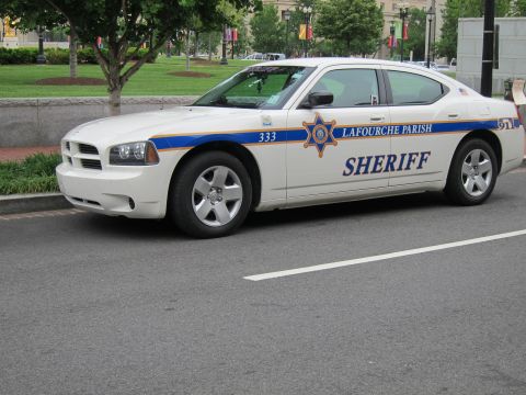1991 Ford LTD Crown Victoria - white Dodge Charger sheriff car lettered Lafourche Parish Sheriff parked along an urban street with green lawn behind.