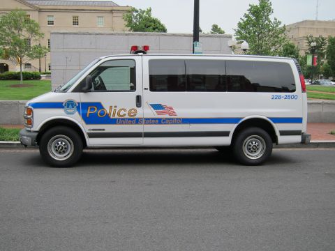 1991 Ford LTD Crown Victoria - white Chevrolet Express police van lettered United States Capitol Police parked along a curb by a stone wall.