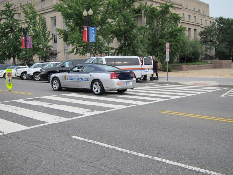 1991 Ford LTD Crown Victoria - silver State Police Dodge Charger stopped at a crosswalk near other patrol cars and a large government building.