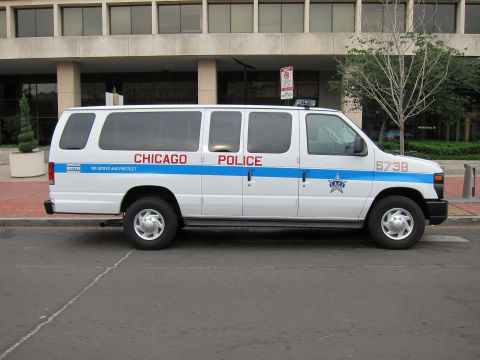1991 Ford LTD Crown Victoria - Side profile of a white Chicago Police Ford Econoline van with a blue stripe parked along a street.