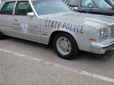 1991 Ford LTD Crown Victoria - Close side-front view of a silver Rhode Island State Police sedan with door shield emblem in a parking lot.