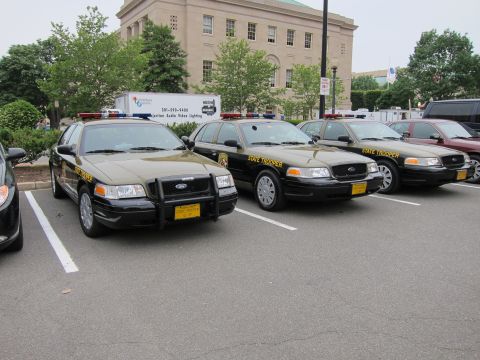 1991 Ford LTD Crown Victoria - Several black-and-tan State Trooper Ford Crown Victoria sedans parked in a row in a lot by a building.
