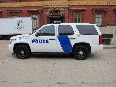 1991 Ford LTD Crown Victoria - white Chevrolet Tahoe police SUV marked Homeland Security Federal Protective Service Police, parked beside a box truck.
