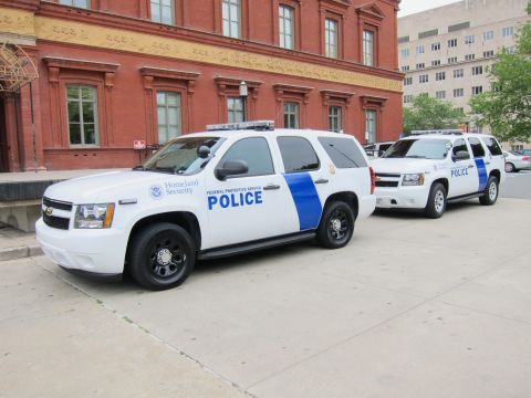 1991 Ford LTD Crown Victoria - Two white Chevrolet Tahoe Homeland Security Federal Protective Service Police SUVs parked nose-to-tail along a brick building.