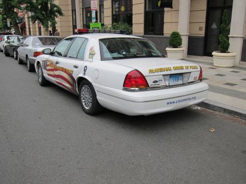 1991 Ford LTD Crown Victoria - Rear of a white Ford Crown Victoria marked Fraternal Order of Police and ctstatefop.org, parked in a line of cars on a city street.