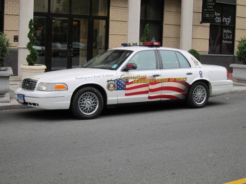 1991 Ford LTD Crown Victoria - white Ford Crown Victoria with American flag side graphics marked Connecticut Fraternal Order of Police, parked on a city street.