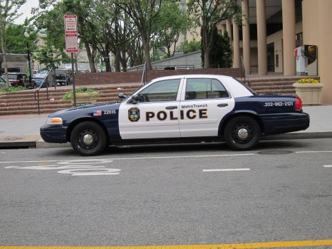1991 Ford LTD Crown Victoria - black-and-white Ford Crown Victoria marked Metro Transit Police, unit 22615, parked at a curb near a tree-lined plaza.