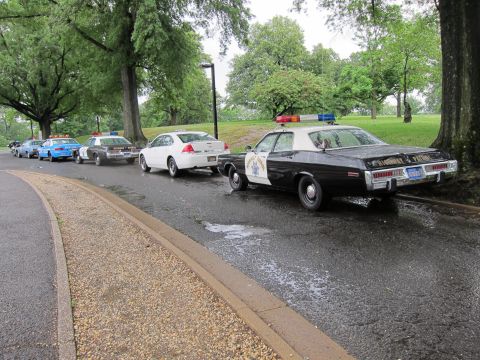1991 Ford LTD Crown Victoria - Rear view of several classic patrol cars lined up on a wet park road, led by a black-and-white Highway Patrol sedan.