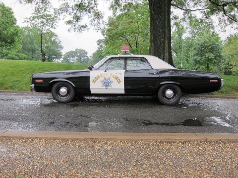 1991 Ford LTD Crown Victoria - Side profile of a vintage black-and-white Highway Patrol sedan with a single red roof light parked on a wet park road.