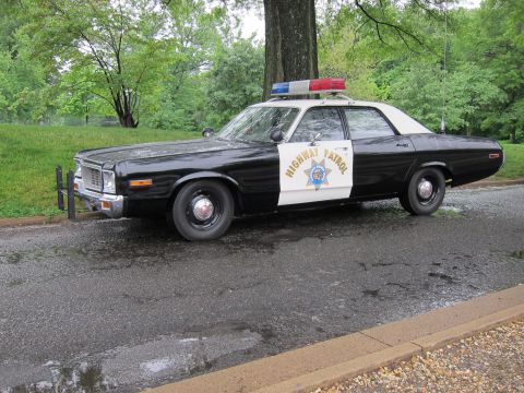 1991 Ford LTD Crown Victoria - vintage black-and-white Highway Patrol sedan with a roof light bar parked beside a large tree on a wet park road.