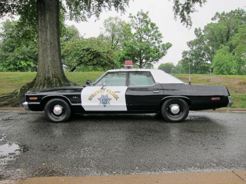 1991 Ford LTD Crown Victoria - Side view of a classic black-and-white Highway Patrol sedan with a door shield emblem parked on a wet tree-lined road.