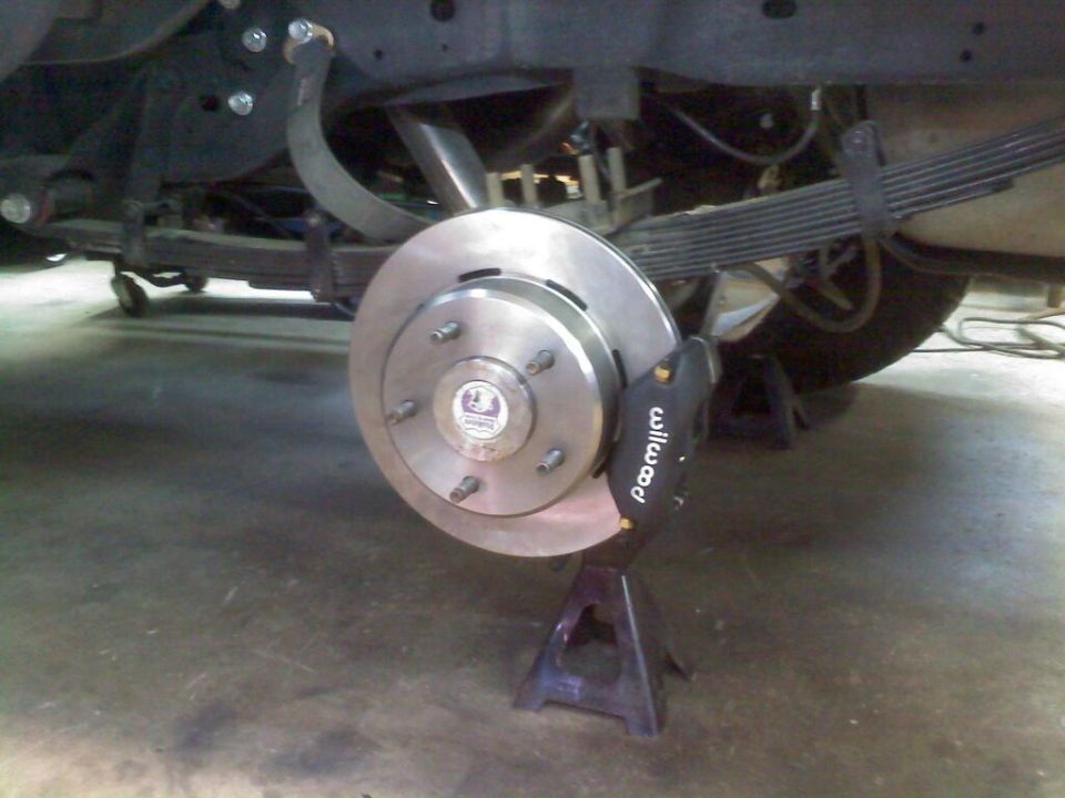 Close-up of a vehicle's rear brake rotor and caliper assembly, supported by jack stands