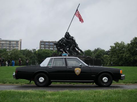 1991 Ford LTD Crown Victoria - all-black police sedan with roof light parked on grass before the Iwo Jima Marine Corps War Memorial.