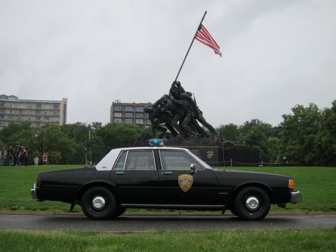 1991 Ford LTD Crown Victoria - black police sedan with door shield emblem parked on grass in front of the Iwo Jima Marine Corps War Memorial.