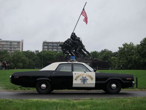 1991 Ford LTD Crown Victoria - black-and-white Highway Patrol sedan parked on grass in front of the Iwo Jima Marine Corps War Memorial and US flag.