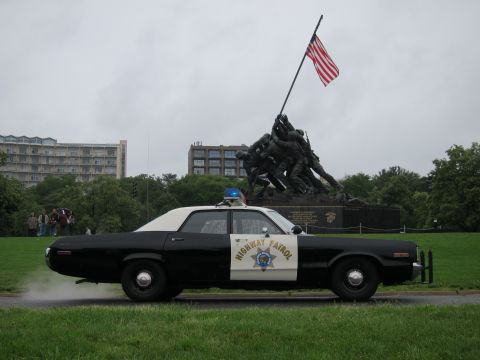 1991 Ford LTD Crown Victoria - black-and-white Highway Patrol sedan emitting exhaust smoke parked before the Iwo Jima Marine Corps War Memorial.