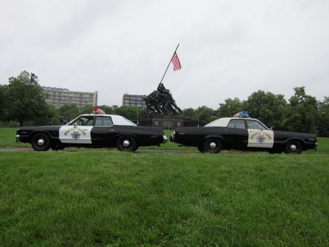 1991 Ford LTD Crown Victoria - Two black-and-white Highway Patrol sedans parked nose-to-nose on grass before the Iwo Jima Marine Corps War Memorial.