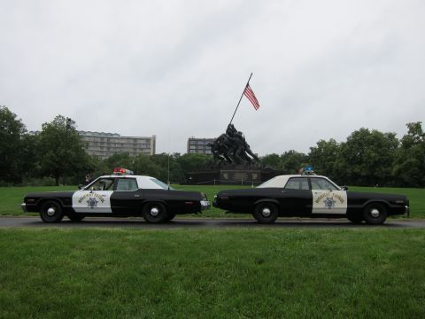 1991 Ford LTD Crown Victoria - Two vintage black-and-white Highway Patrol sedans parked nose-to-nose on grass at the Iwo Jima War Memorial.