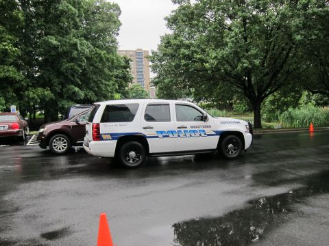 1991 Ford LTD Crown Victoria - white Chevrolet Tahoe police SUV marked POLICE parked behind a maroon SUV on a wet tree-lined road.