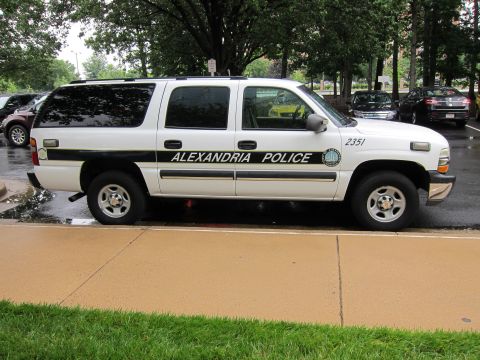 1991 Ford LTD Crown Victoria - white Chevrolet Suburban marked ALEXANDRIA POLICE 2351 parked at a curb on a wet street.