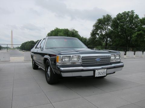 1991 Ford LTD Crown Victoria - black Ford four-door sedan sits on a stone plaza with the Washington Monument visible in the cloudy background.