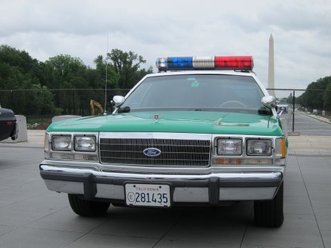 1991 Ford LTD Crown Victoria - Front view of a green-and-white Ford police sedan with a roof lightbar and California plate, Washington Monument behind.