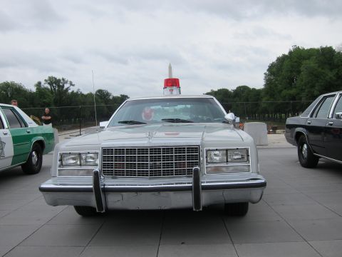 1991 Ford LTD Crown Victoria - Head-on view of a silver four-door sedan fitted with a single red roof beacon, parked on a plaza near the Washington Monument.