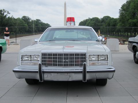 1991 Ford LTD Crown Victoria - Head-on view of a silver sedan with a red roof beacon parked near the Washington Monument under overcast skies.