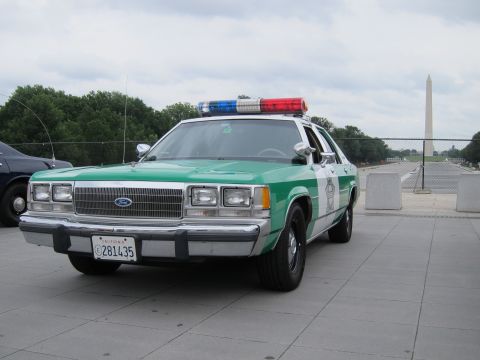 1991 Ford LTD Crown Victoria - green-and-white Ford police sedan with a roof lightbar parked on a stone plaza, the Washington Monument in the distance.
