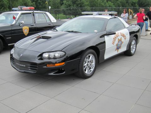 1991 Ford LTD Crown Victoria - black-and-white Chevrolet Camaro marked Highway Patrol with a roof lightbar, parked on a plaza beside other police cars.