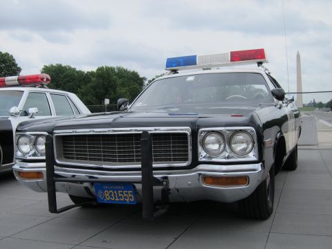 1991 Ford LTD Crown Victoria - Front view of a black-and-white Dodge police sedan with a push bar, roof lightbar and California plate, Washington Monument behind.