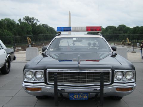 1991 Ford LTD Crown Victoria - Head-on view of a black-and-white Dodge police sedan with push bar and roof lightbar, the Washington Monument centered behind.