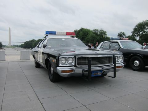 1991 Ford LTD Crown Victoria - Front three-quarter view of a black-and-white Dodge police sedan with push bar and lightbar, Washington Monument in the distance.