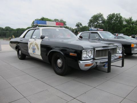 1991 Ford LTD Crown Victoria - Front three-quarter view of a black-and-white Highway Patrol sedan with roof lightbar, parked among other cars on a plaza.