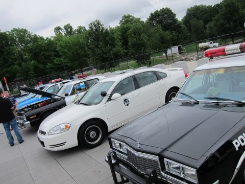 1991 Ford LTD Crown Victoria - white Chevrolet Impala police car parked among other police vehicles on a plaza, a black cruiser in the foreground.