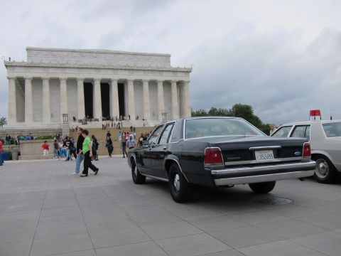 1991 Ford LTD Crown Victoria - dark Ford sedan on the Lincoln Memorial plaza beside a police cruiser as pedestrians pass by.