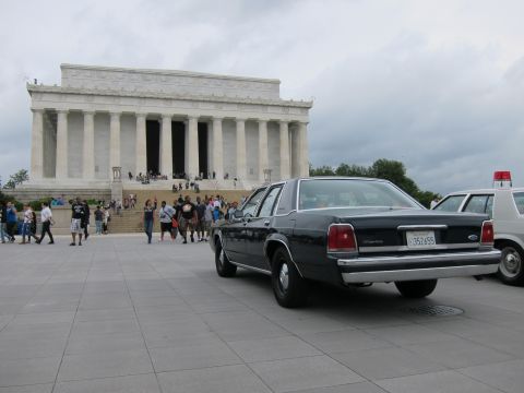 1991 Ford LTD Crown Victoria - dark Ford sedan parked next to a white police cruiser on the plaza in front of the Lincoln Memorial.