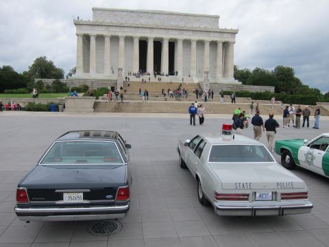 1991 Ford LTD Crown Victoria - dark Ford sedan and a white STATE POLICE cruiser parked on the plaza before the Lincoln Memorial steps.