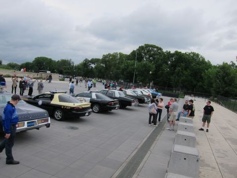 1991 Ford LTD Crown Victoria - line of police vehicles including a black-and-tan FHP Camaro parked on a plaza as people stand nearby.