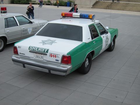 1991 Ford LTD Crown Victoria - green-and-white SHERIFF Ford Crown Victoria parked beside a Rhode Island state police car on a plaza.