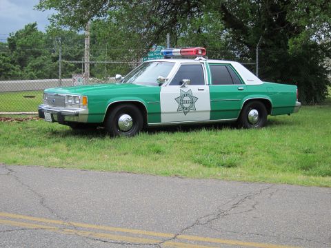 1991 Ford LTD Crown Victoria - green and white Ford sheriff sedan with red and blue roof lights parked at the edge of a road.